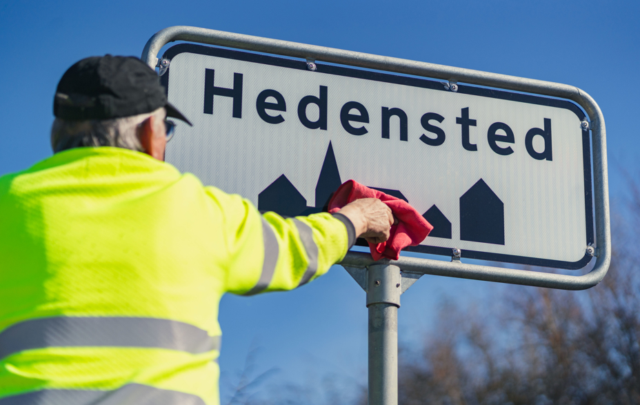 En kommunaltansat pudser et byskilt i Hedensted.